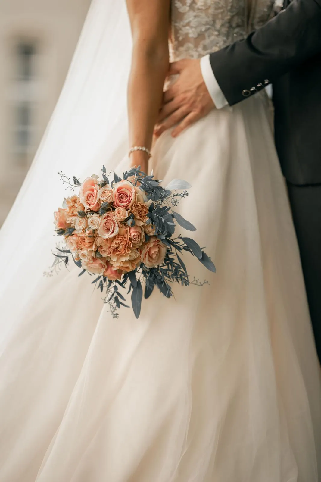 Brautstrauß mit pfirsichfarbenen Rosen vor einem Brautkleid